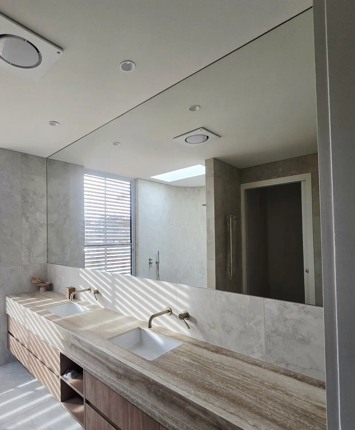 Large frameless mirror fitted above a stone bathroom vanity