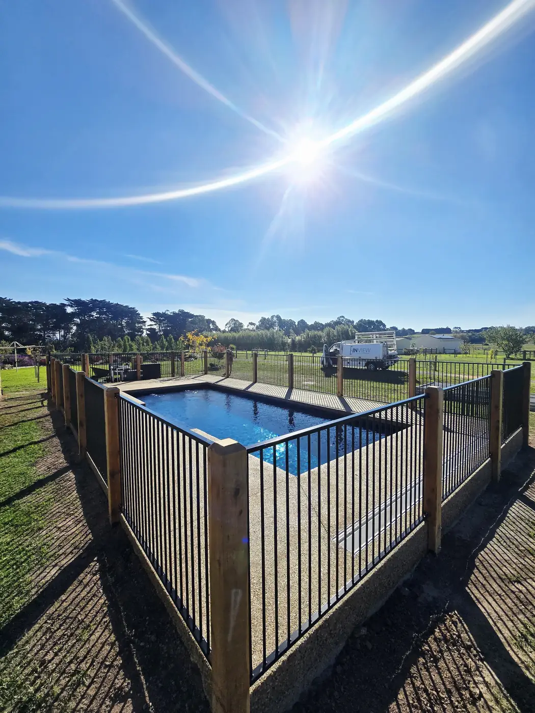 Black aluminium pool fence with timber posts around a backyard swimming pool