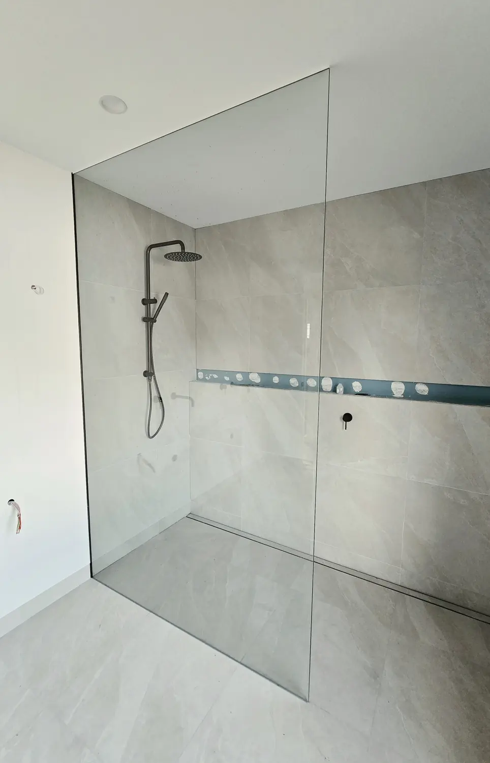 Frameless shower screen panel in a grey tiled bathroom