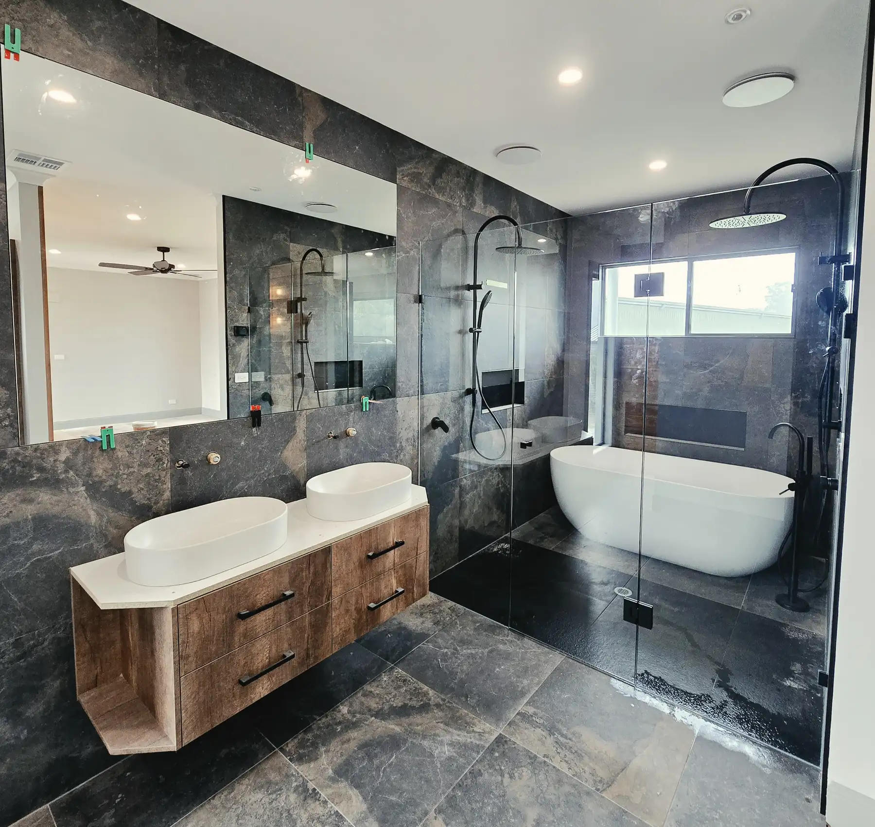 Frameless shower screen and large mirror in a dark stone bathroom with a freestanding bath