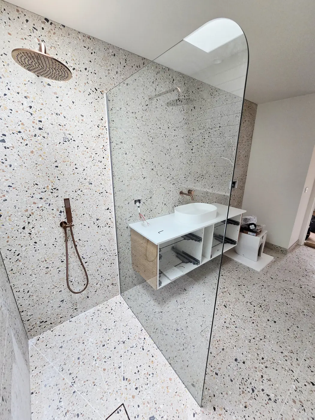 Frameless shower screen with a curved top edge against a terrazzo wall